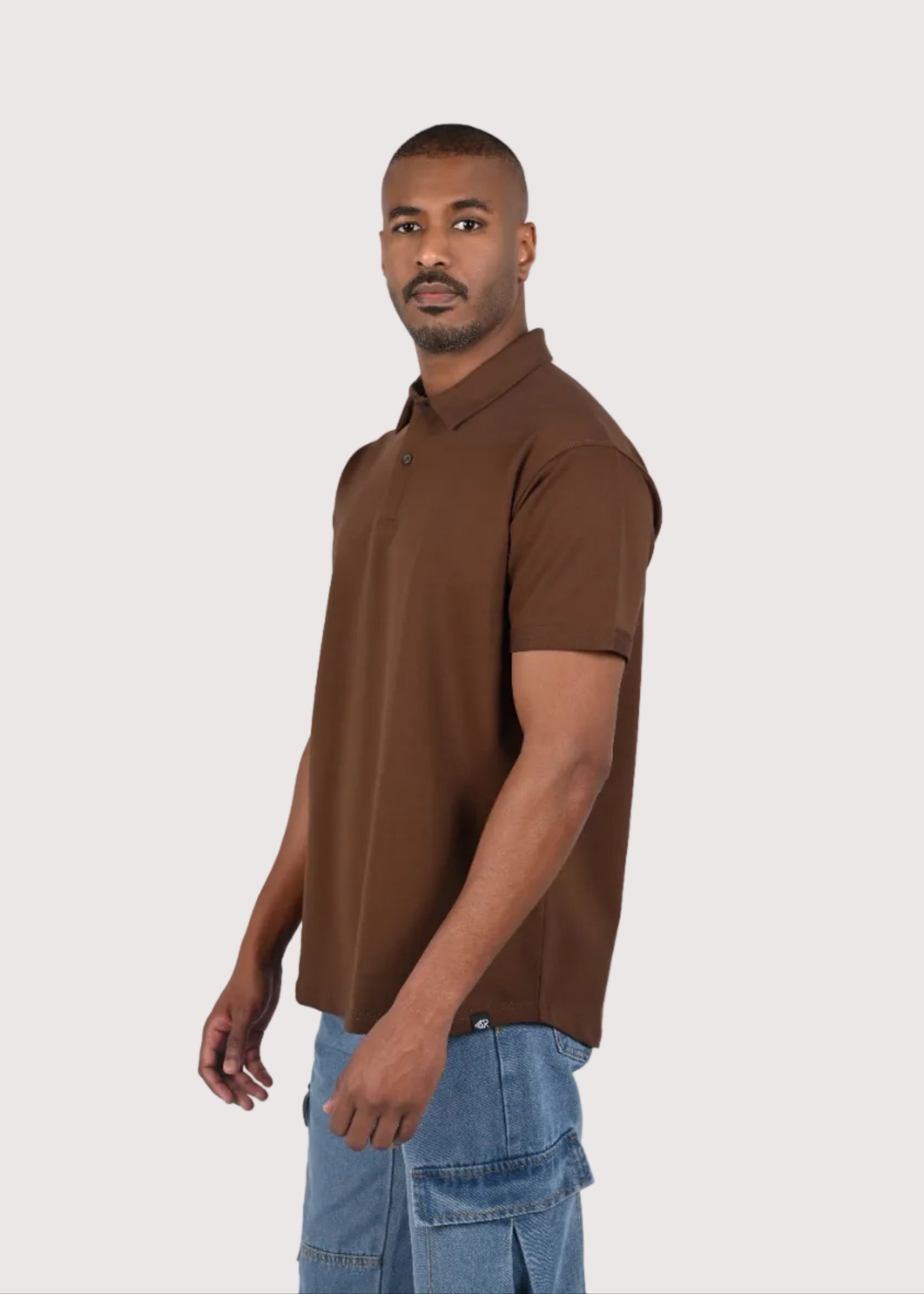 Man wearing a brown polo shirt and blue jeans on a white background